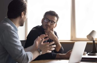 dwóch mężczyzn siedzących przy stole przy laptopie